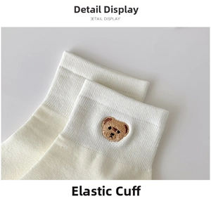 Close-up of white cotton ankle socks featuring cute bear embroidery and elastic rib cuff
