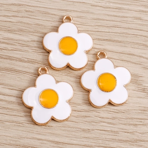 Close-up of three daisy charms with white petals and gold trim on wood background