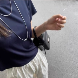 Long collier chaîne serpent argentée porté avec un t-shirt marine et pantalon blanc