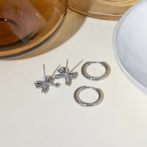 Detailed view of silver bow studs and small hoop earrings on a minimalist background