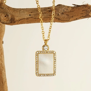 Golden stainless steel rectangle pendant necklace with white shell and crystals on wood