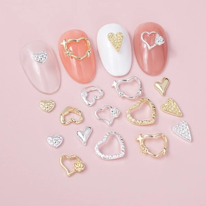 Mixed heart-shaped nail art charms in gold and silver with rhinestones on pink background