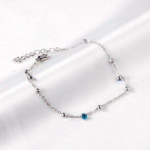 Detailed shot of silver evil eye bracelet with blue beads on white silk background