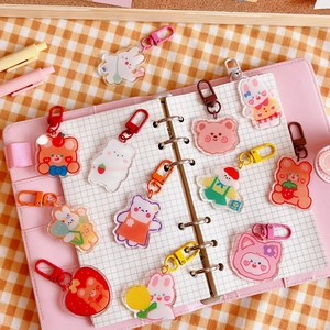 Cute acrylic cartoon bear and bunny charms displayed on a pink notebook with clips