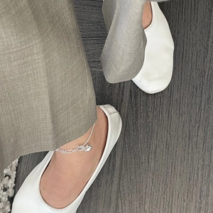 Macro view of sterling silver heart anklet worn with white flat shoes and grey pants