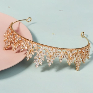 Close-up of golden bridal crown with leaf-shaped zircon tassels on a pink stand