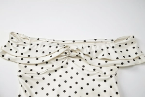 Detail of off-shoulder neckline with ruffle trim and twist knot on white polka dot dress