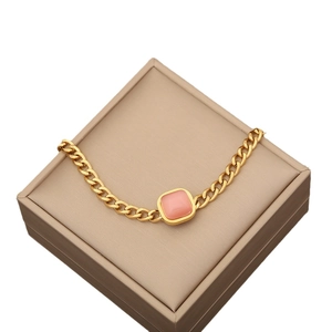 Pink square cat eye stone pendant on golden cuban chain necklace in a beige jewelry box