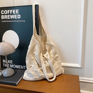 Close-up of the cream knitted tote bag showing intricate cable knit textures on wood