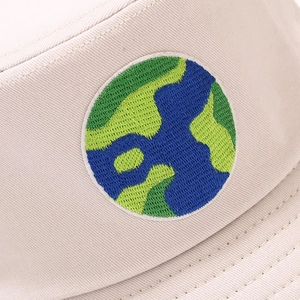 Macro shot of embroidered earth patch on a light beige bucket hat with fine fabric texture