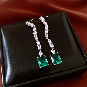 Detail of silver drop earrings with emerald green stones and pavé crystals on a black box