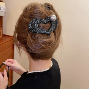 Detail of a black glitter heart-shaped claw clip with a grey pearl on the edge