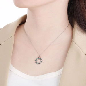 Close-up of a silver Christmas wreath pendant necklace worn by a model in a beige blazer