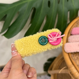 Detail of yellow plush hair clip with green and pink buttons and a cute bow tie