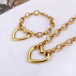 Detailed view of chunky gold chain jewelry set with hollow heart charms on white fabric
