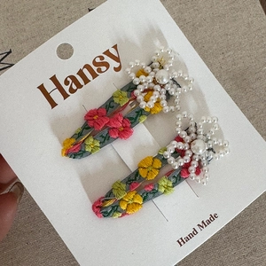 Floral embroidery hair clips with pearl flower accents on a grey textured background