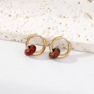 Detail of gold hoop earrings with dark red marble stone charms on a textured stone base