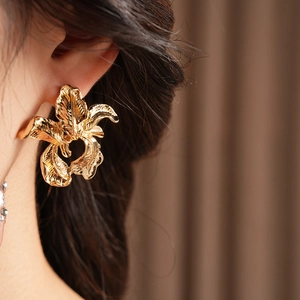 Close-up of model wearing large golden irregular flower earrings in polished metal