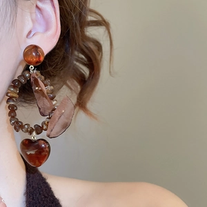 Close-up of a brown resin beaded hoop earring with silk leaves and heart-shaped pendant