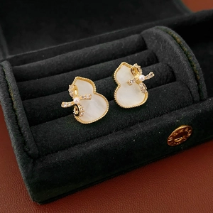 Detailed view of gourd-shaped gold earrings with white shell and bowknot in a velvet box