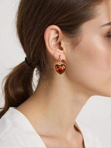 Détail d'une boucle d'oreille cœur dorée en résine ambrée, vue rapprochée sur un mannequin