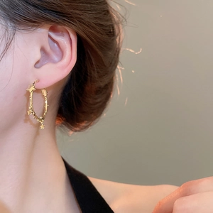 Close-up of a model wearing golden hoop earrings with multiple star pendants