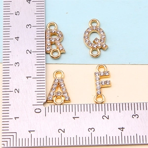 Detailed measurement of gold rhinestone alphabet charms with a ruler for size reference