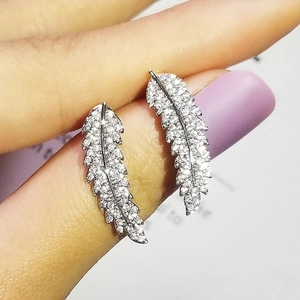 Macro shot of silver feather earrings with zircon inlay held between fingers
