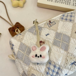Close-up of white plush rabbit charm with embroidered details on a quilted canvas bag