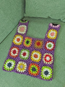 Close-up of handmade crochet tote bag with colorful granny square patterns on purple base