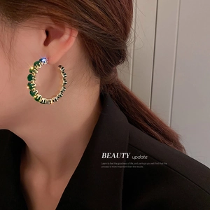 Elegant gold hoop earrings with green zircon stones worn by a model in black suit