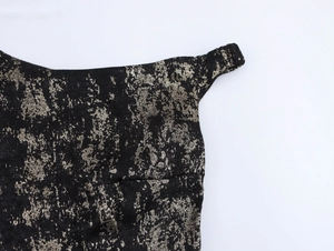 Close-up of black dress fabric with metallic gold texture and thin shoulder strap