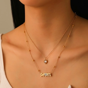 Detail of layered gold stainless steel necklace with MOM pendant and small heart charm