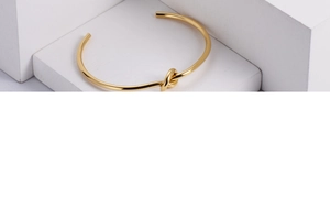 Close-up of minimalist gold knot cuff bracelet on a white geometric display stand