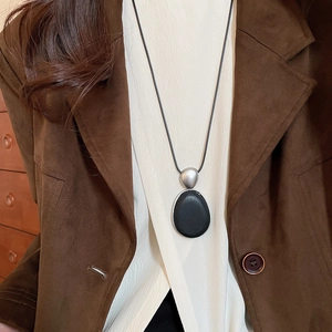 Détail du pendentif ovale minimaliste en bois sur un long collier en cordon noir sobre