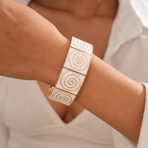 Detailed close-up of geometric square bracelet with white enamel and golden spiral textures