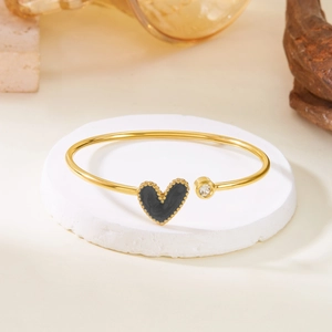 Detail of gold open heart bangle with black enamel pendant and sparkling zircon stone