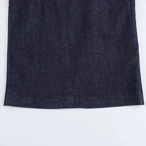 Gros plan détaillé sur la texture du denim indigo et l'ourlet cousu de la robe midi