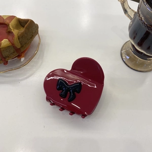 Detail shot of heart-shaped burgundy acetate hair claw with a black bow on white table