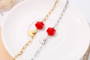 Close-up of gold and silver heart bracelets with red faceted beads on a ceramic plate