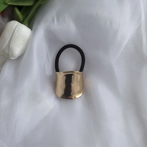 Detail of a shiny gold metal lava-style hair cuff with black elastic on white fabric