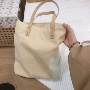 Detail view of cream canvas tote bag with light brown leather straps and rivet accents