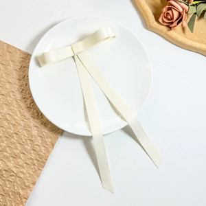 Detail view of ivory satin bow hair clip with long ribbons on a white ceramic plate