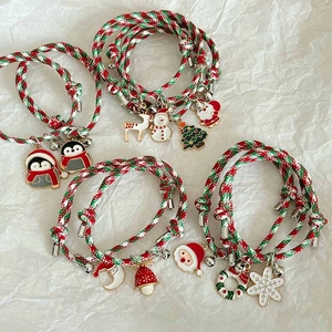 Adjustable Christmas themed braided bracelets with festive charms and bells on white paper