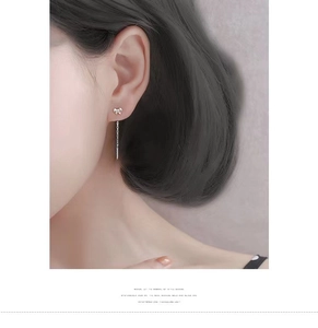 Close-up of minimalist silver bow tassel earrings worn by a model in soft lighting