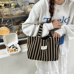 Detail of striped canvas tote bag with woven handles and minimalist brand label