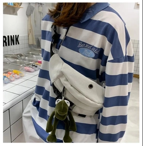 Detail of off-white canvas waist bag with adjustable black strap and green frog plush charm