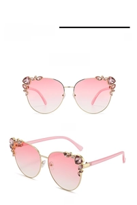 Detail of cat eye sunglasses with gold frames, pink lenses, and rhinestone accents