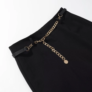 Dettaglio di pantaloni neri con elegante cintura a catena dorata e pendente circolare