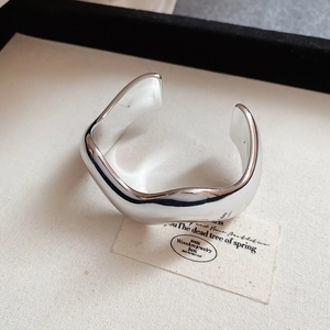 Dettaglio di un bracciale aperto in argento con design ondulato e finitura lucida